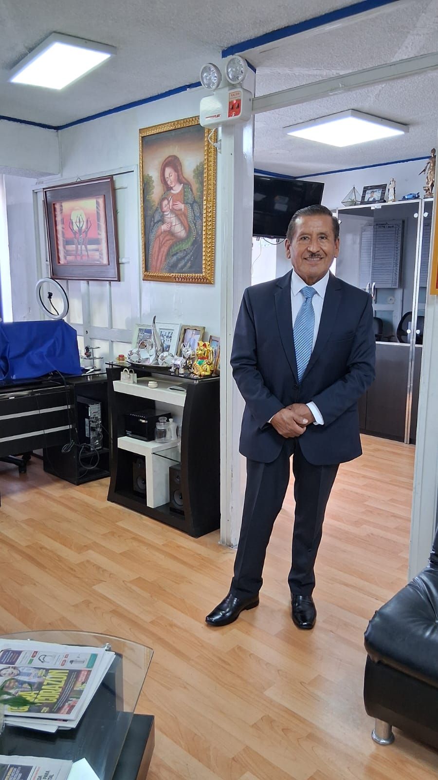 El Dr. Severino Saire de pie en su oficina de San Borja, junto a una pintura colonial de la Virgen