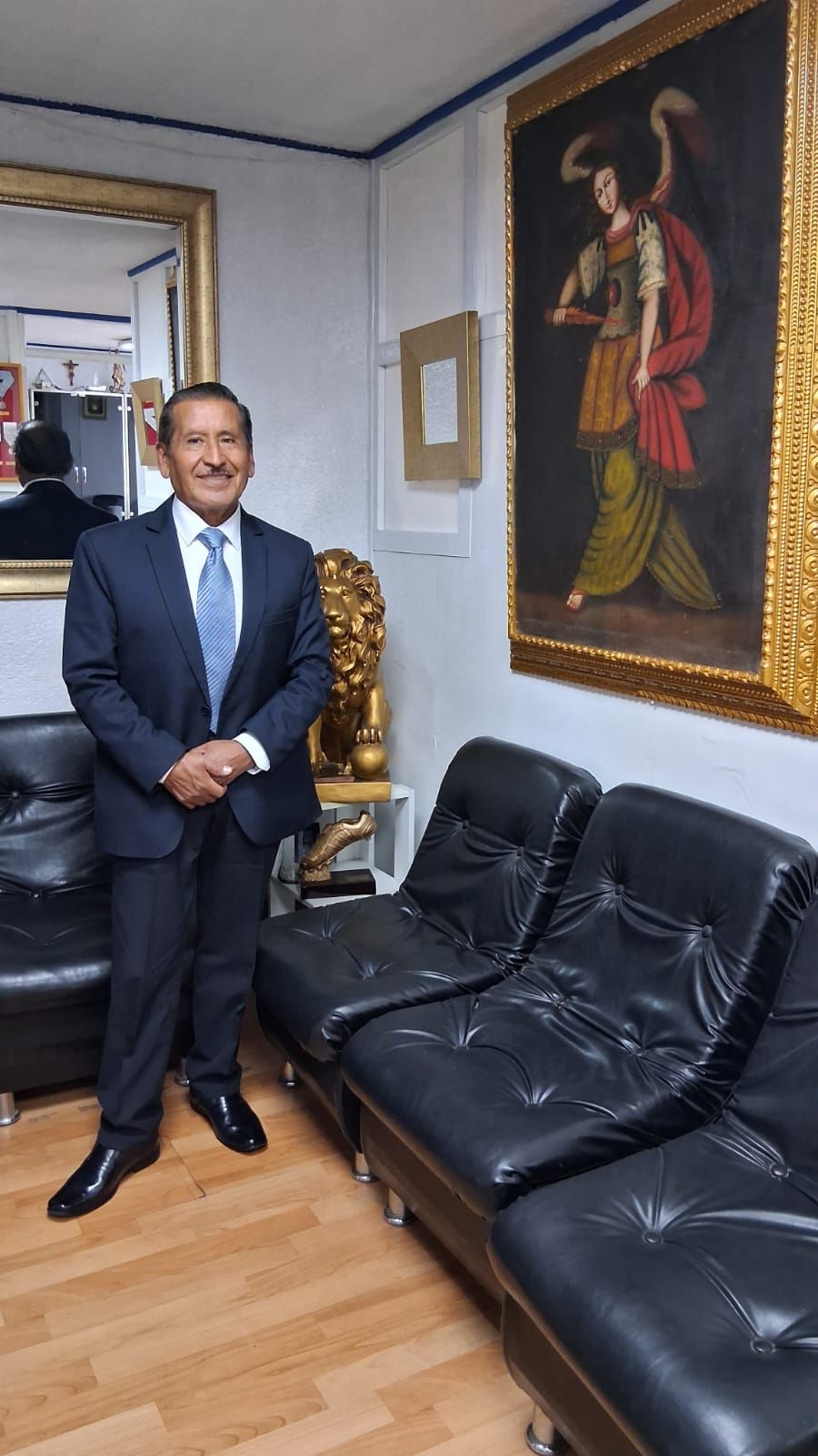 El Dr. Severino Saire en la sala de su estudio, junto a una pintura colonial con marco dorado y un león dorado